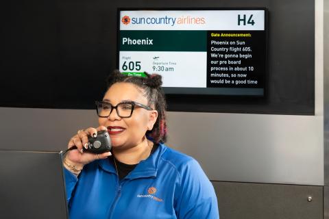 Talk-to-text captures the voice announcement of a Sun Country Airlines agent, who is speaking into a microphone at Gate H4. The announcement is displayed on a screen behind the agent. It reads: "... Phoenix on Sun Country flight 605. We're gonna begin our pre board process in about 10 minutes, so now would be a good time ..."